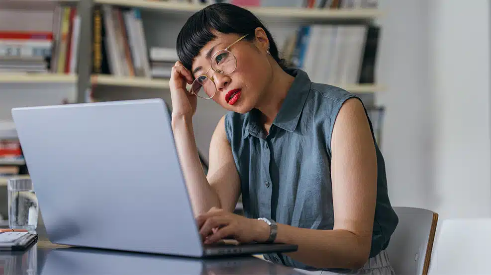 Woman scratching her head, thinking, while looking at the computer screen.